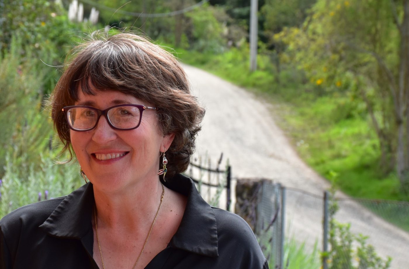 Lynne Klippel smiling outside her home in the Andes, a garden path behind her