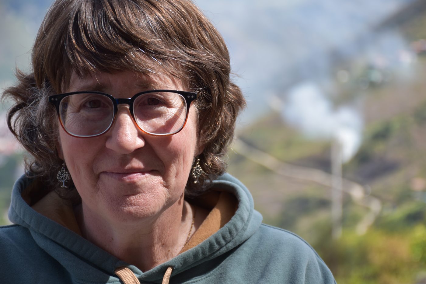Lynne Klippel in a green hoodie and tree earrings, the Andes behind her